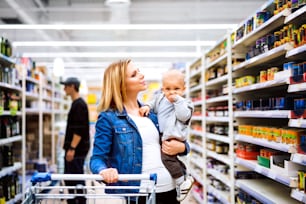 Young mother with her little baby boy at the supermarket, shopping.