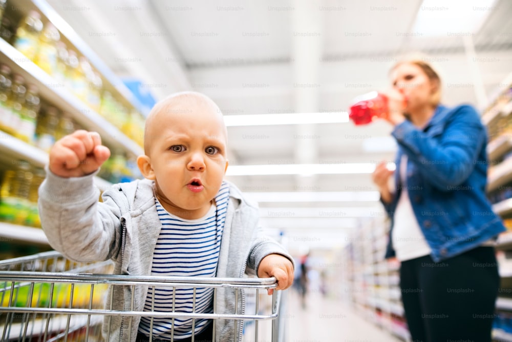 Jovem mãe irreconhecível com seu filhinho no supermercado, fazendo compras.