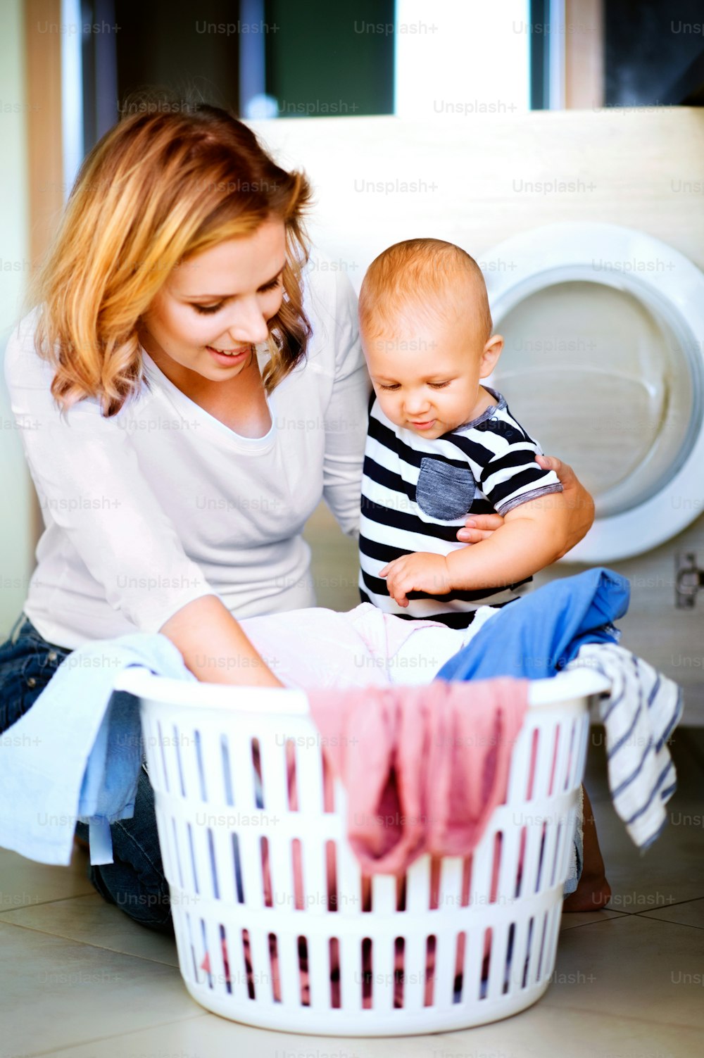 Young mother with a baby son doing housework. Beautiful woman and baby boy doing laundry.
