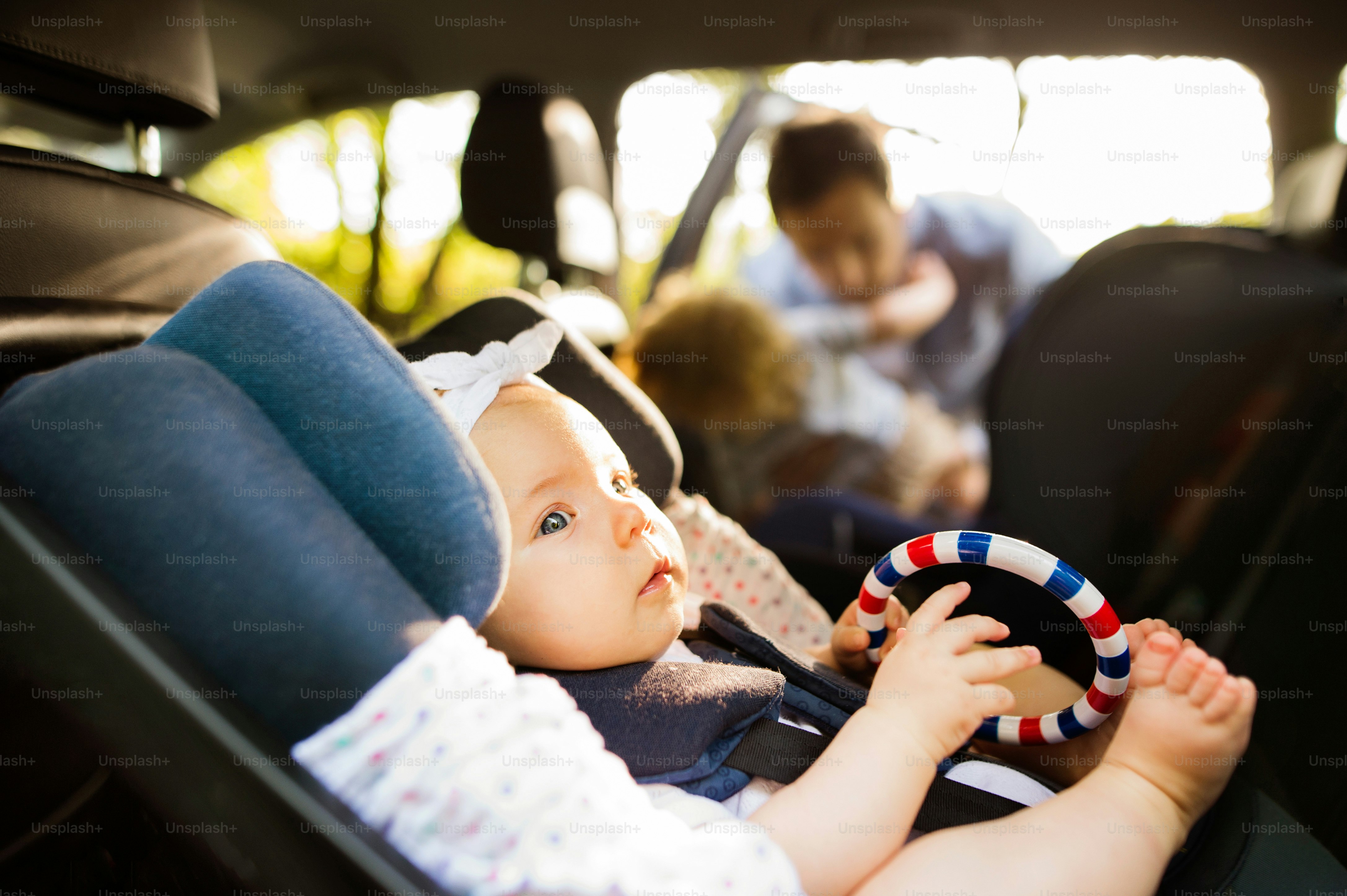 Bayi perempuan kecil yang lucu diikat dengan sabuk pengaman di kursi mobil pengaman.