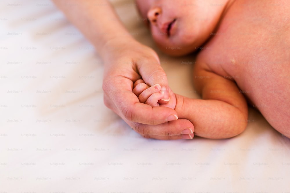 Filha bebê irreconhecível deitada na cama, segurando a mão de sua mãe.
