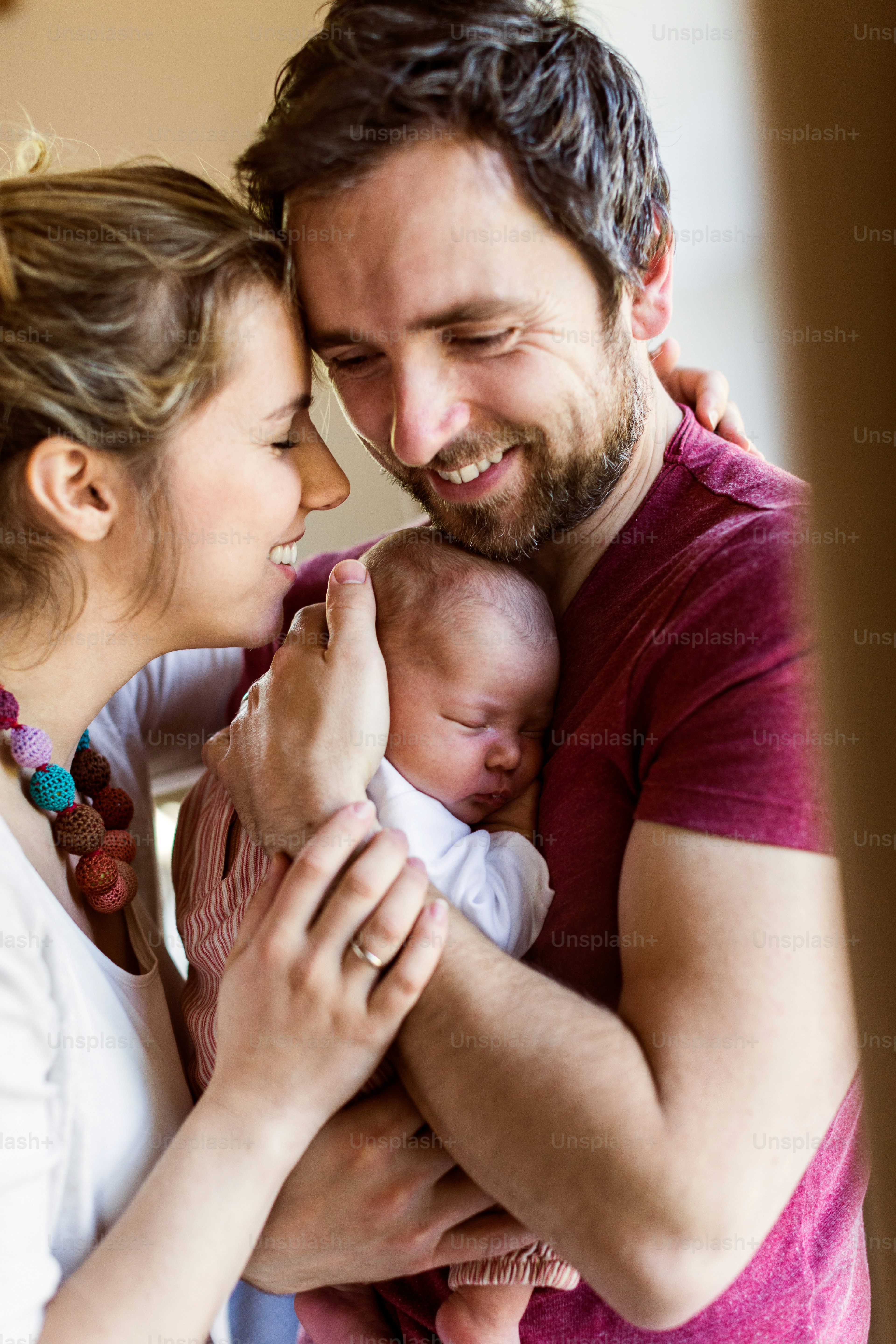 Beautiful young parents at home standing at the window holding their cute baby daughter in the arms