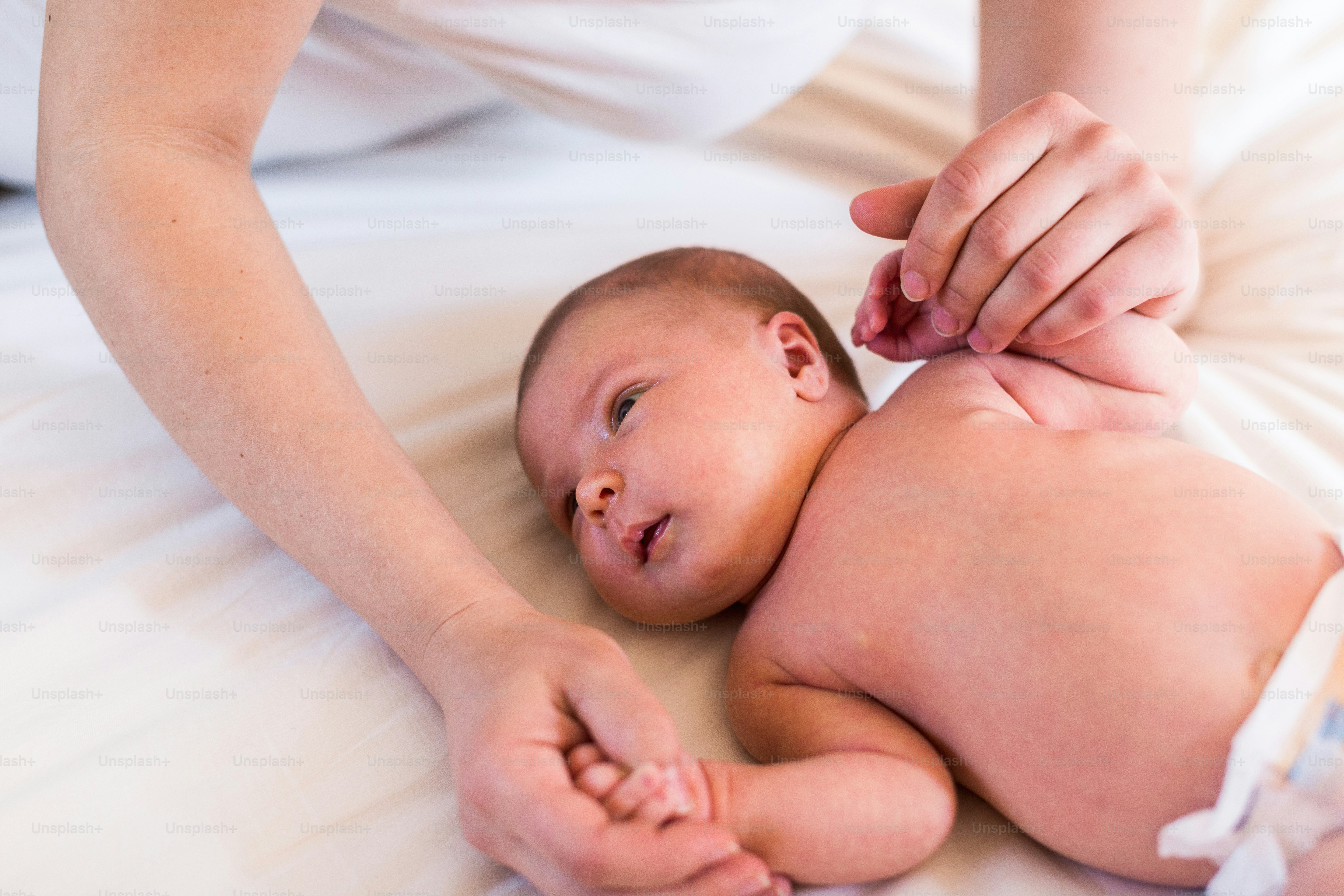 Ibu muda yang tidak dikenali di rumah menggendong bayi perempuannya yang lucu berbaring di tempat tidur.