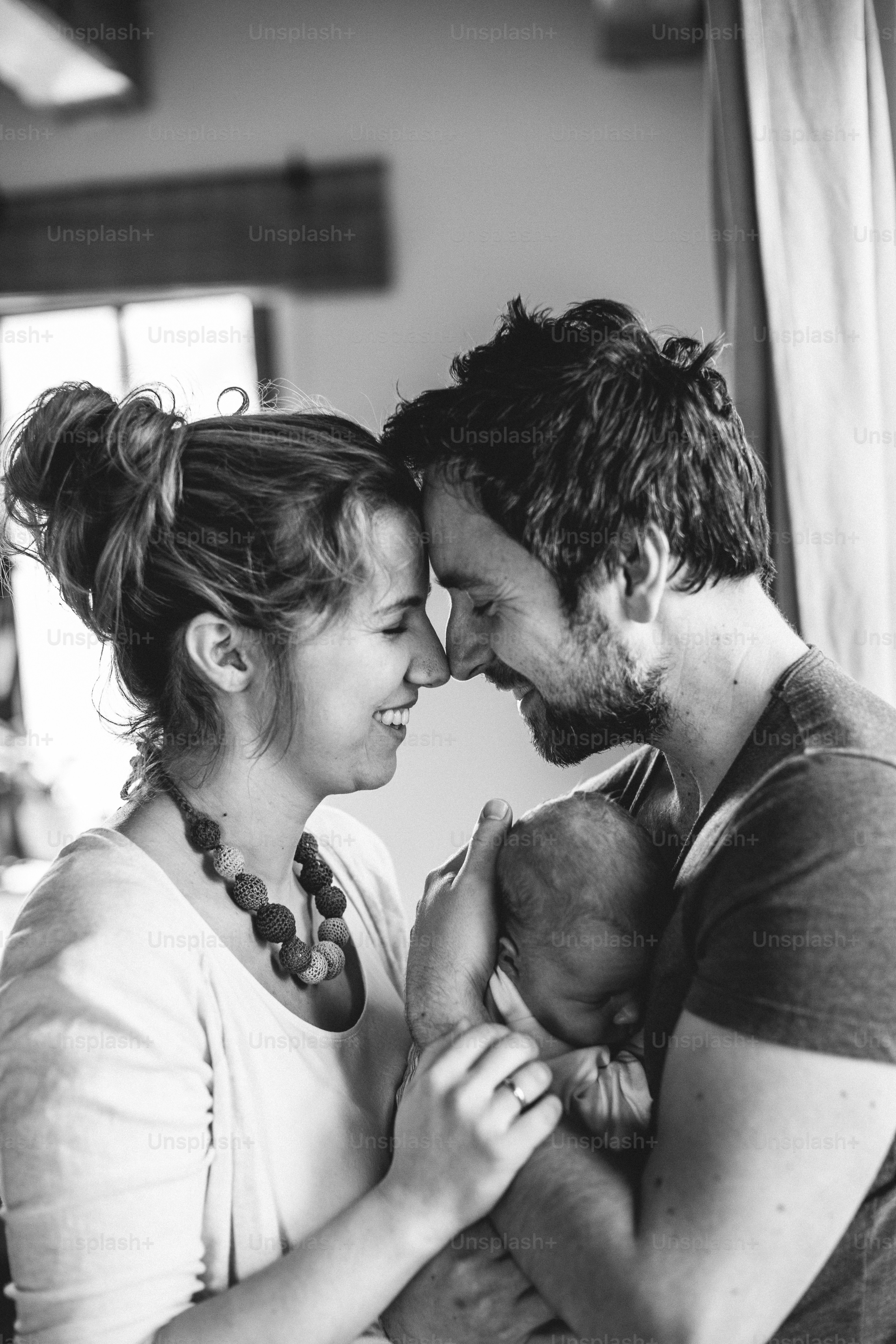 Beautiful young parents at home standing at the window holding their cute baby daughter in the arms.