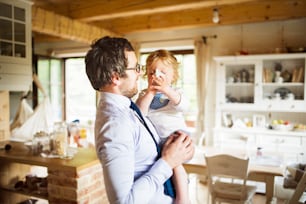 Young businessman coming home from work, in the kitchen with his little son holding him in the arms.
