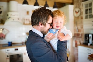 Young businessman coming home from work, holding his little son in the arms.