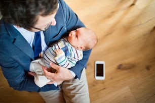 Young businessman at home with his little baby daughter in the arms. Smart phone laid on wooden floor.