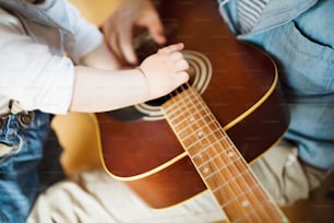 Unrecognizable little boy at home playing guitar with his father. Close up.