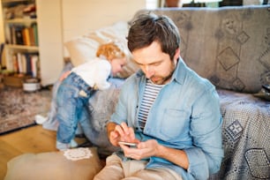 Young father with his little son at home, holding smart phone, writing text message.