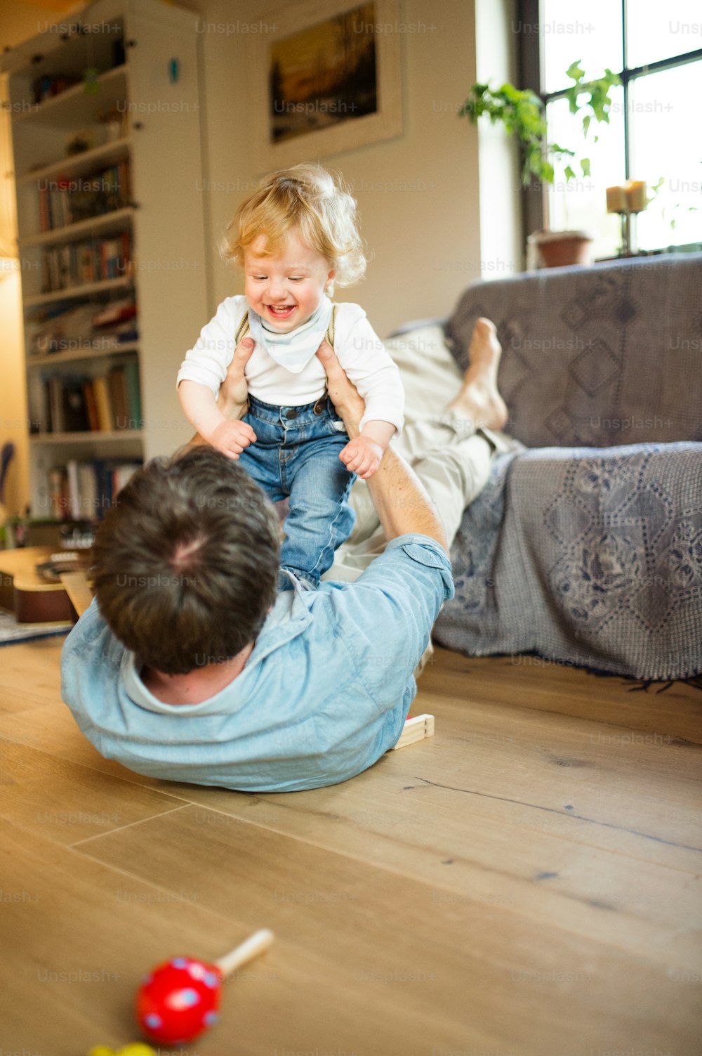 Young father at home lying on wooden floor playing with his little son, cuddling.