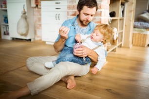 집에 있는 젊은 아버지는 귀여운 아들에게 요구르트를 먹이고 바닥에 앉아 있다.