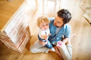 Young father at home sitting on the floor feeding his cute little son with yoghurt.