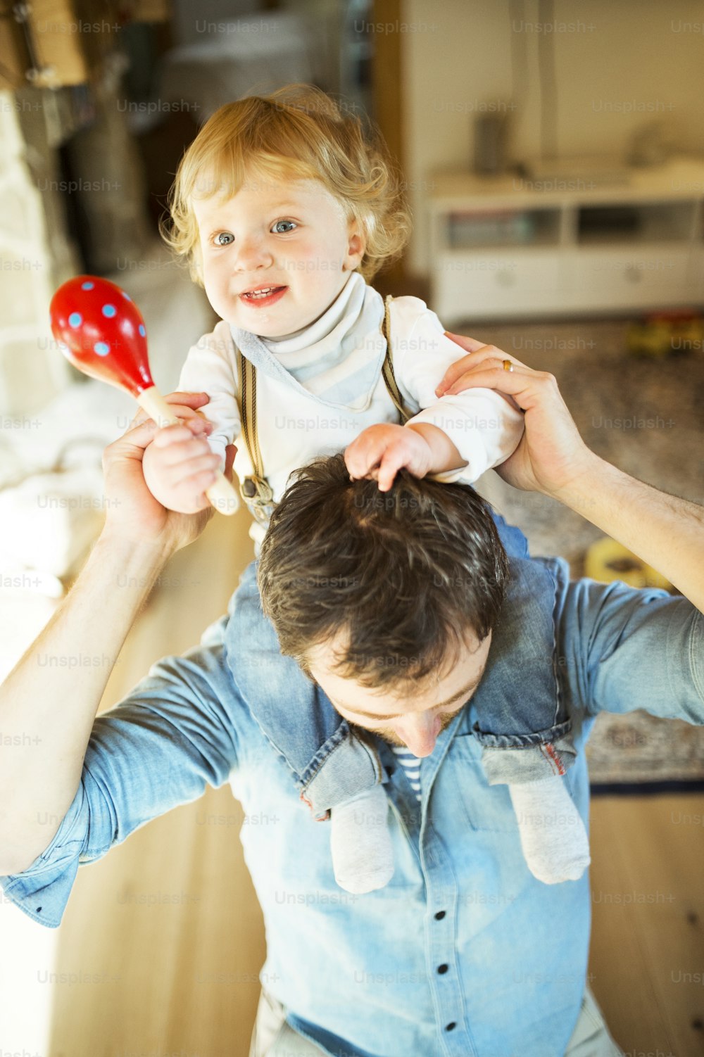 Young father at home giving his little son piggyback, boy playing musical toy.