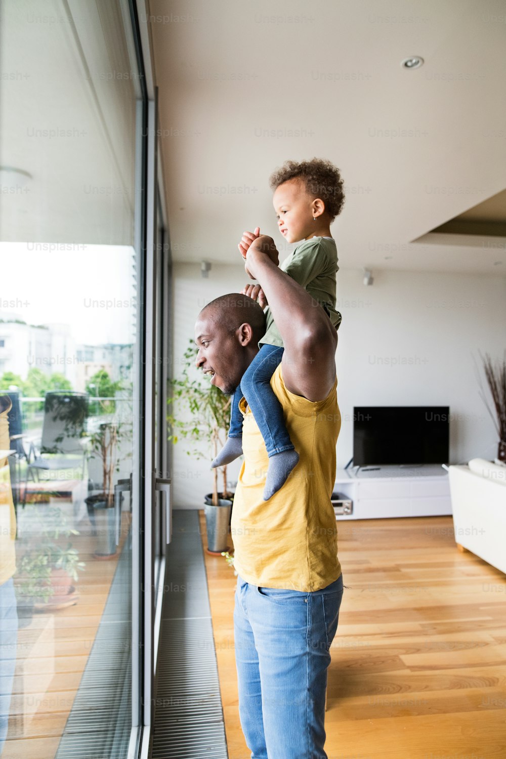 Jeune père afro-américain à la maison à la fenêtre portant sa petite fille sur ses épaules.