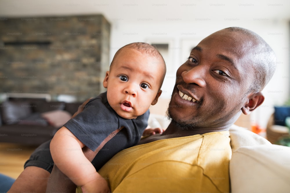 Junger afroamerikanischer Vater zu Hause, der seinen süßen kleinen Sohn in den Armen hält