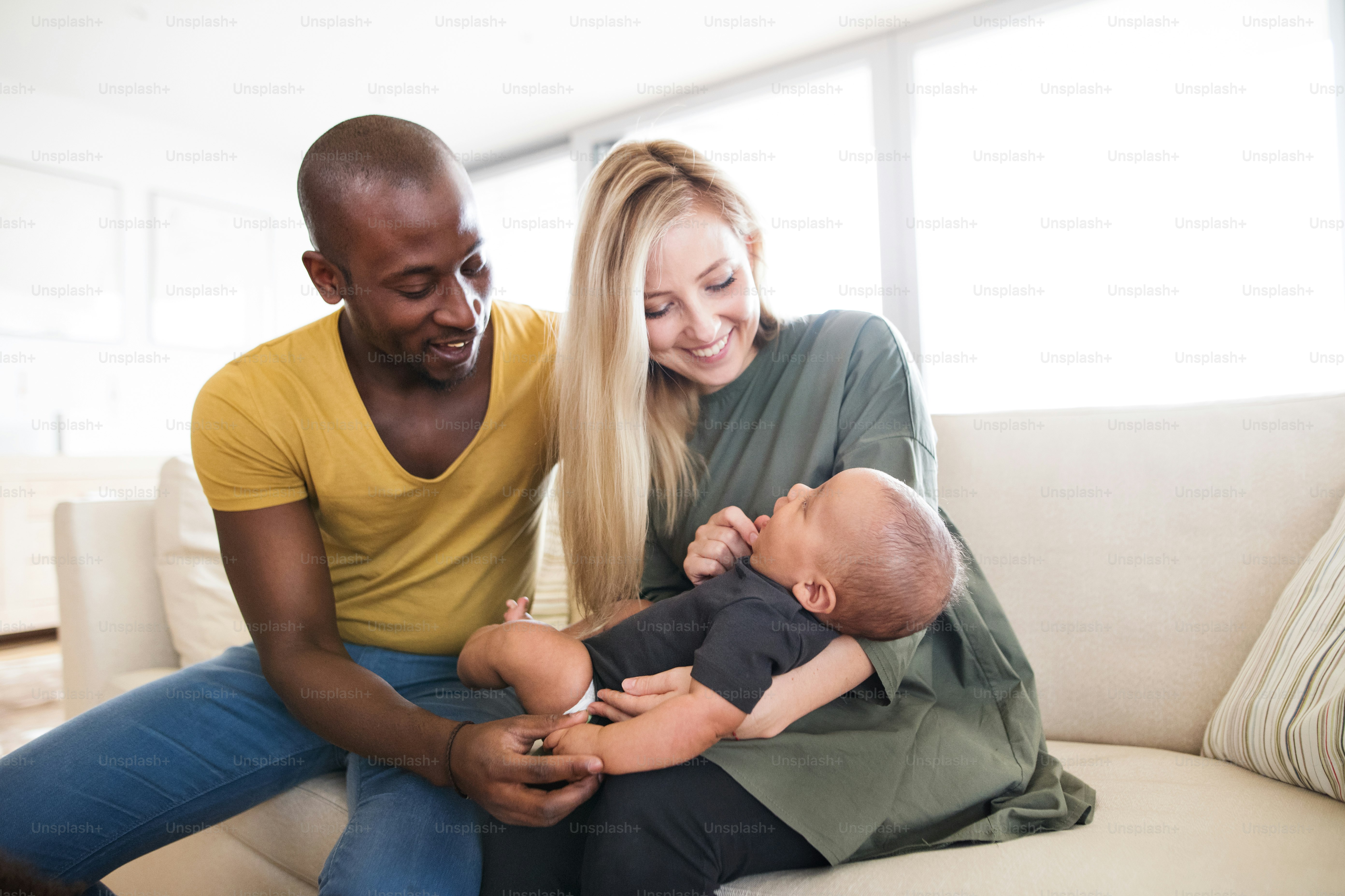 かわいい小さな赤ん坊の息子を抱く家で美しい若い異人種間家族。
