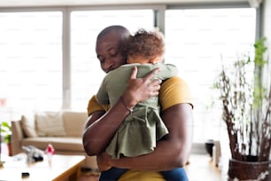 若いアフリカ系アメリカ人の父親が家で、かわいい娘を腕に抱きしめ、抱きしめています。