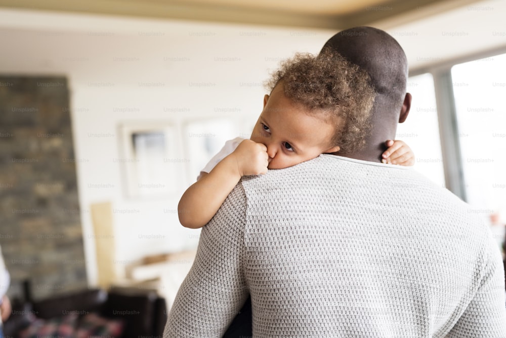 Unrecognizable young afro-american father at home with his cute little daughter holding her in the arms.