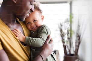 Close up of young afro-american father at home with his cute little daughter holding her in the arms.