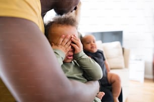 Unrecognizable young afro-american father at home holding his cute little daughter in the arms, his baby son next to him held by his mother