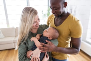Hermosa familia interracial joven en casa sosteniendo a su lindo bebé.