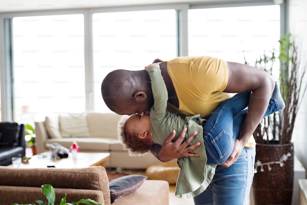 Young afro-american father at home with his cute little daughter holding her in the arms, kissing her.