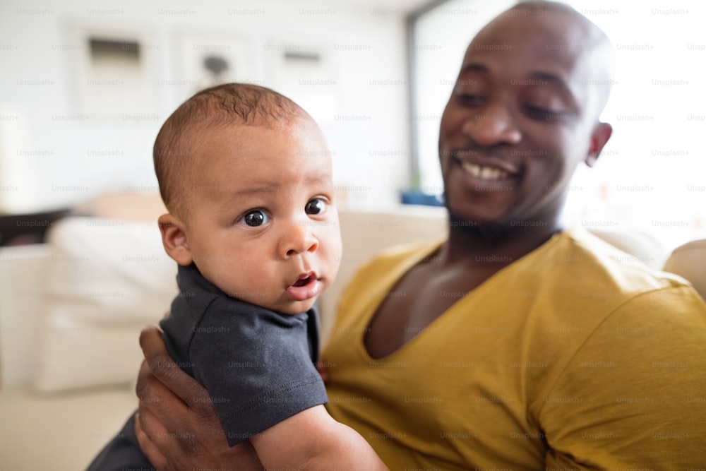 Young afro-american father at home holding his cute baby son in his arms