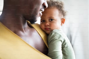 Irreconocible joven padre afroamericano en casa con su linda hijita sosteniéndola en los brazos.