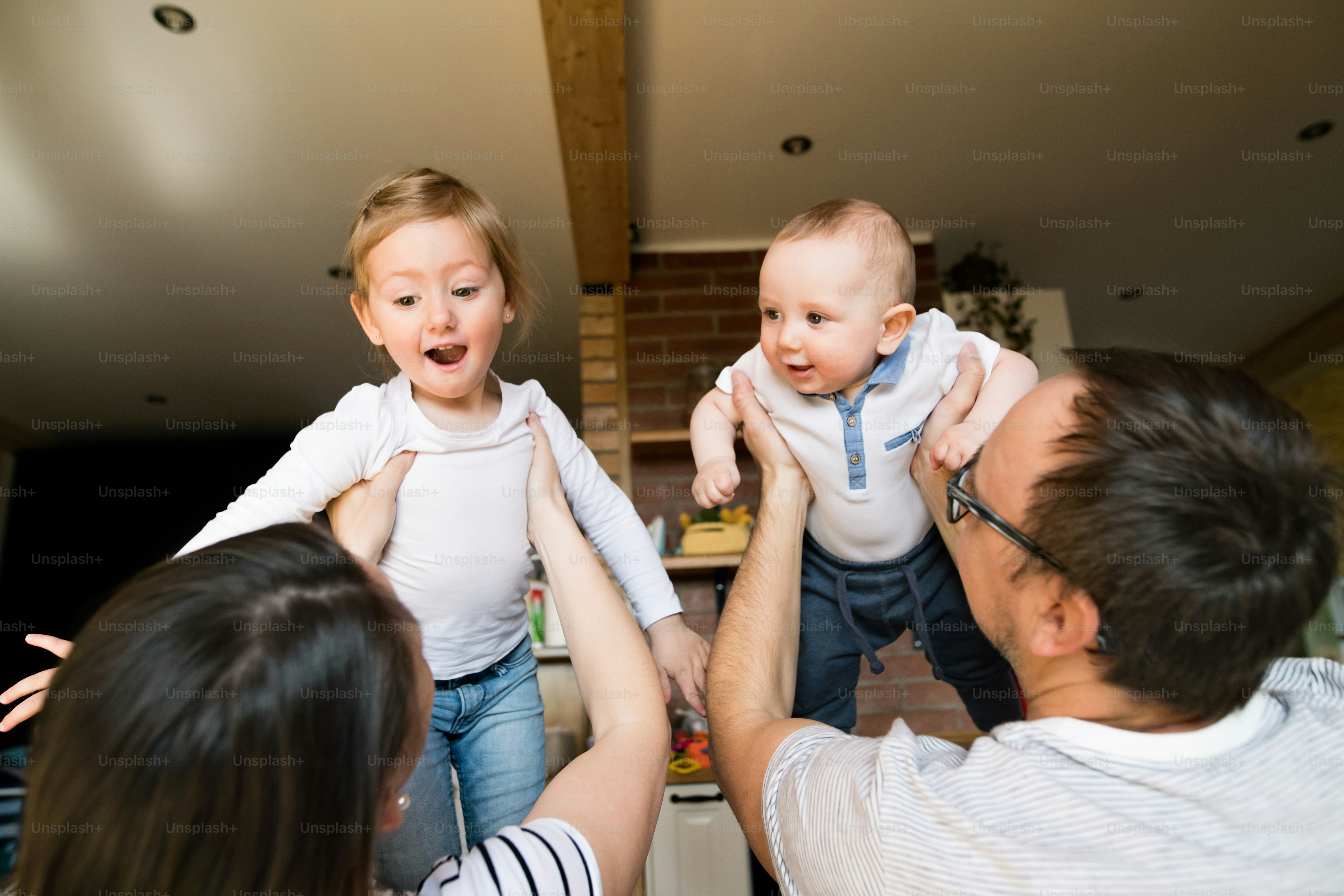 Beautiful young parents at home holding their cute baby son and daughter in the arms.