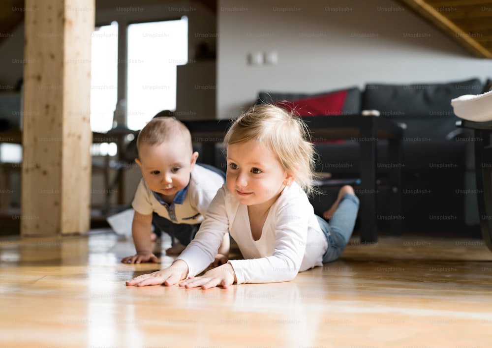 Cute little girl with her baby brother lying on the floor, crawling.