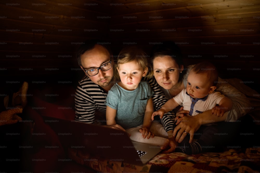 Young parents at home at night with their little children watching something on laptop.