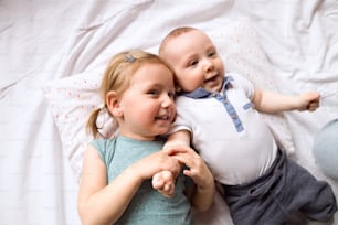 Cute little girl with her baby brother lying on bed together, smiling.