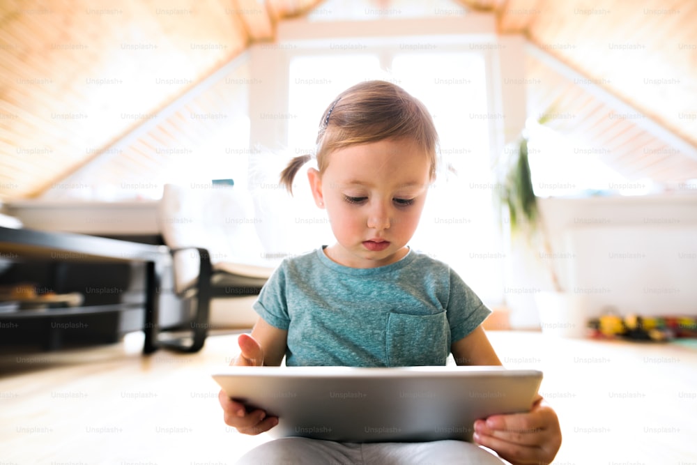 Cute little girl at home sitting on the floor watching something on tablet.