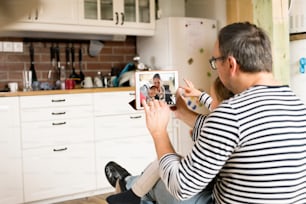 Young father at home with daughter videochatting with mother with baby son on digital tablet.