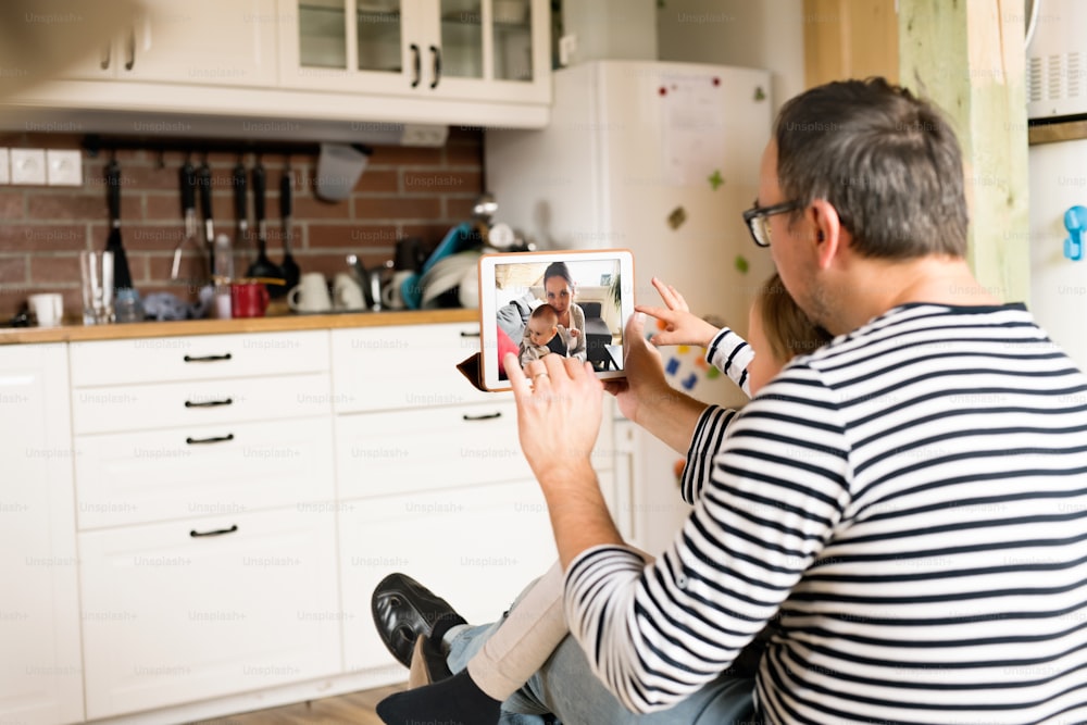 Young father at home with daughter videochatting with mother with baby son on digital tablet.