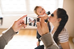 Marido tomando foto con teléfono inteligente de su hermosa y joven esposa y su linda hijita.