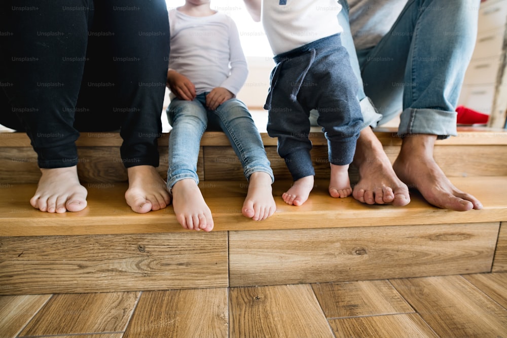 Beautiful young family sitting on stairs. Close up of bare feet of mother, father, daughter and son.