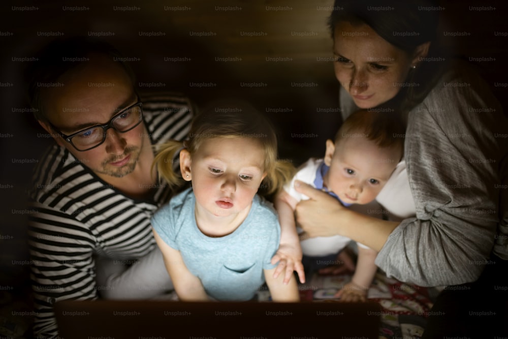 Young parents at home at night with their little children watching something on laptop.