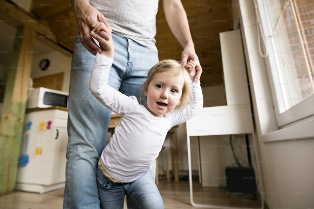 Unrecognizable young father at home holding hands of his cute little daughter.