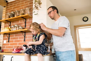 귀여운 딸이 머리를 손질하는 집에 있는 젊은 아버지.
