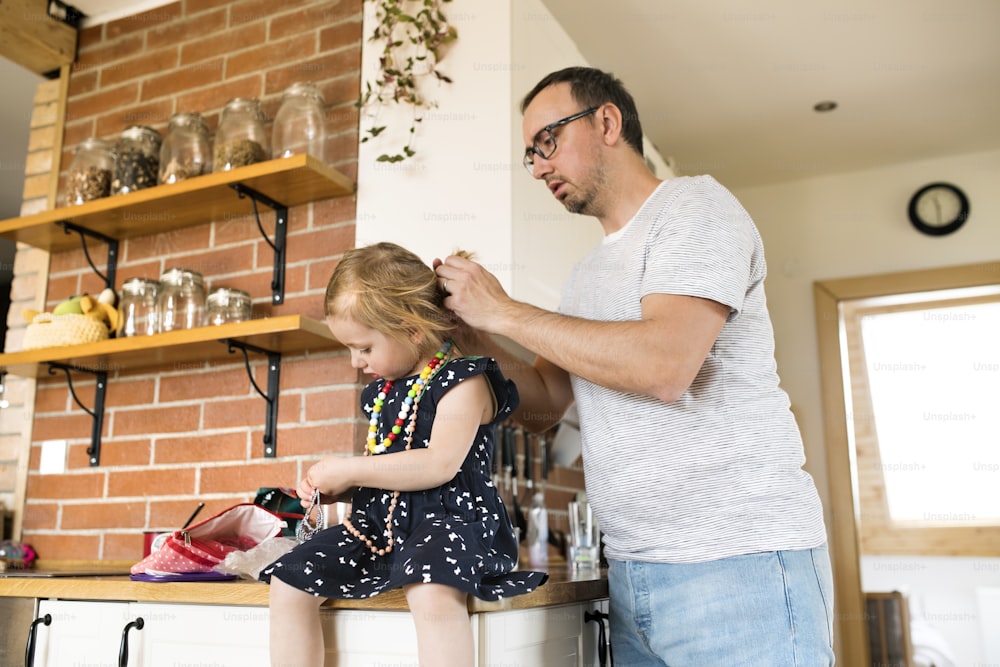 Young father at home with his cute little daughter styling her hair.