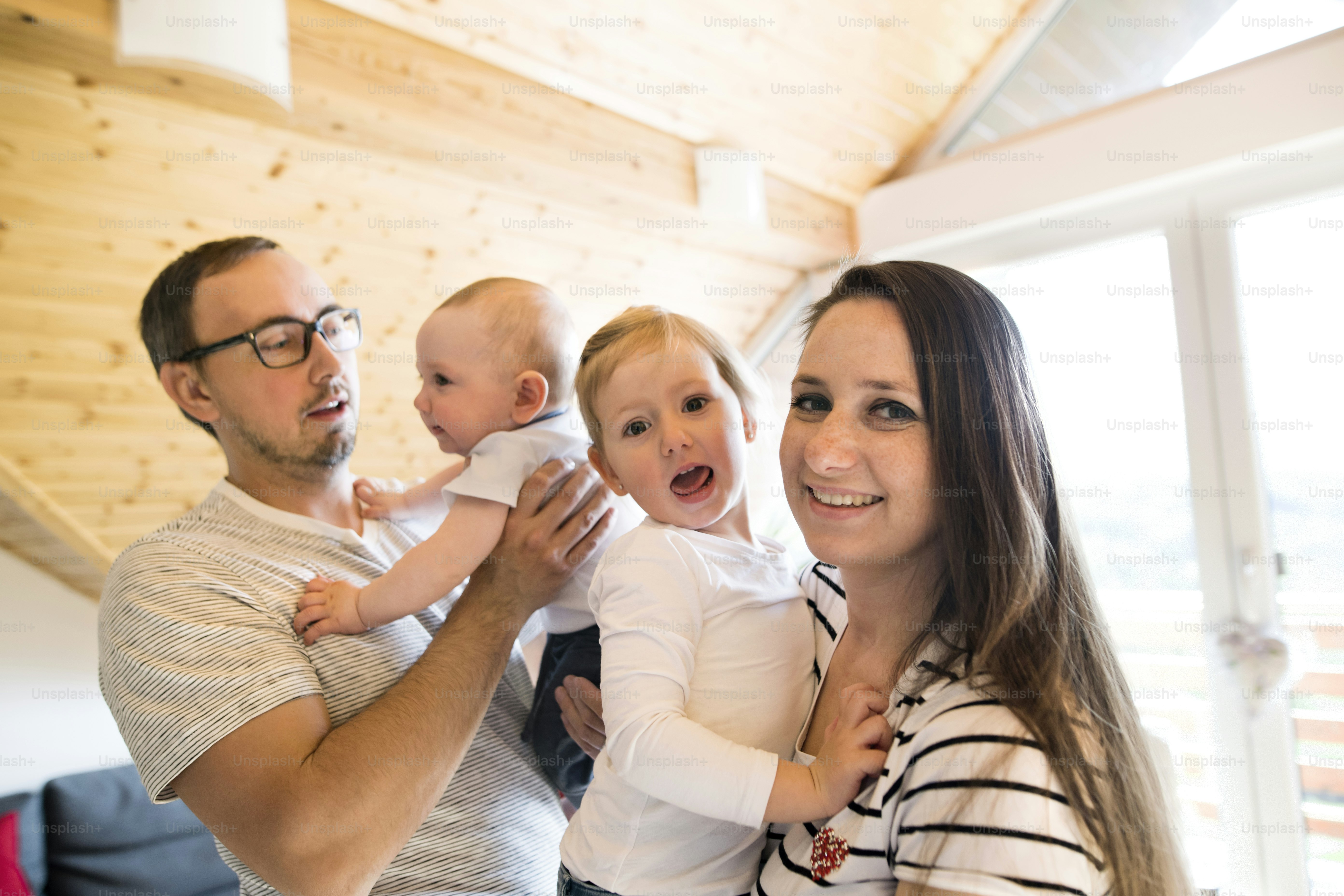 Beautiful young parents at home holding their cute baby son and daughter in the arms.