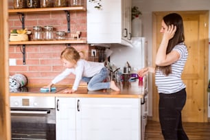 Beautiful young mother at home and her cute little daughter on kitchen countertop.