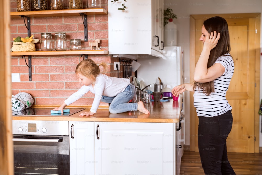 Schöne junge Mutter zu Hause und ihre süße kleine Tochter auf Küchenarbeitsplatte.
