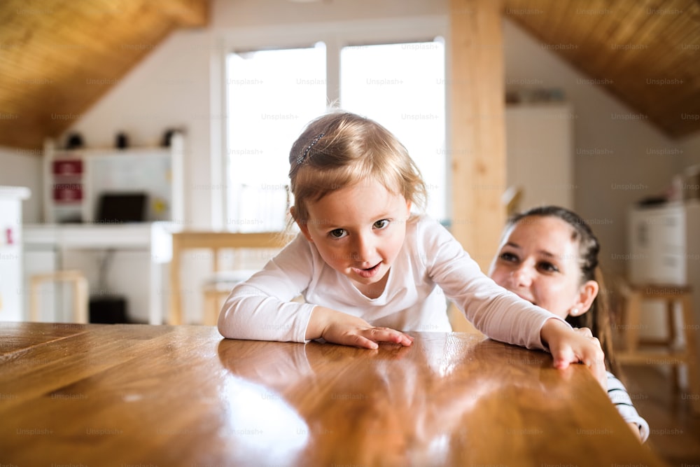 Beautiful young mother at home and her cute little daughter climbing on kitchen countertop.