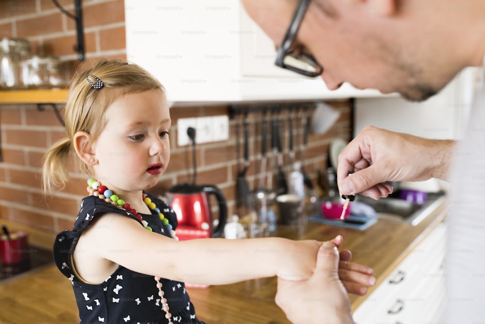 Padre joven con su linda hijita en casa pintándose las uñas.