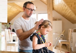 Jeune père à la maison avec sa mignonne petite fille lui faisant une coiffure.