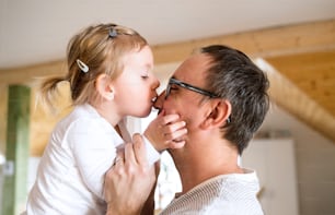 Junger Vater zu Hause mit seiner süßen kleinen Tochter, die ihn auf die Nase küsst.
