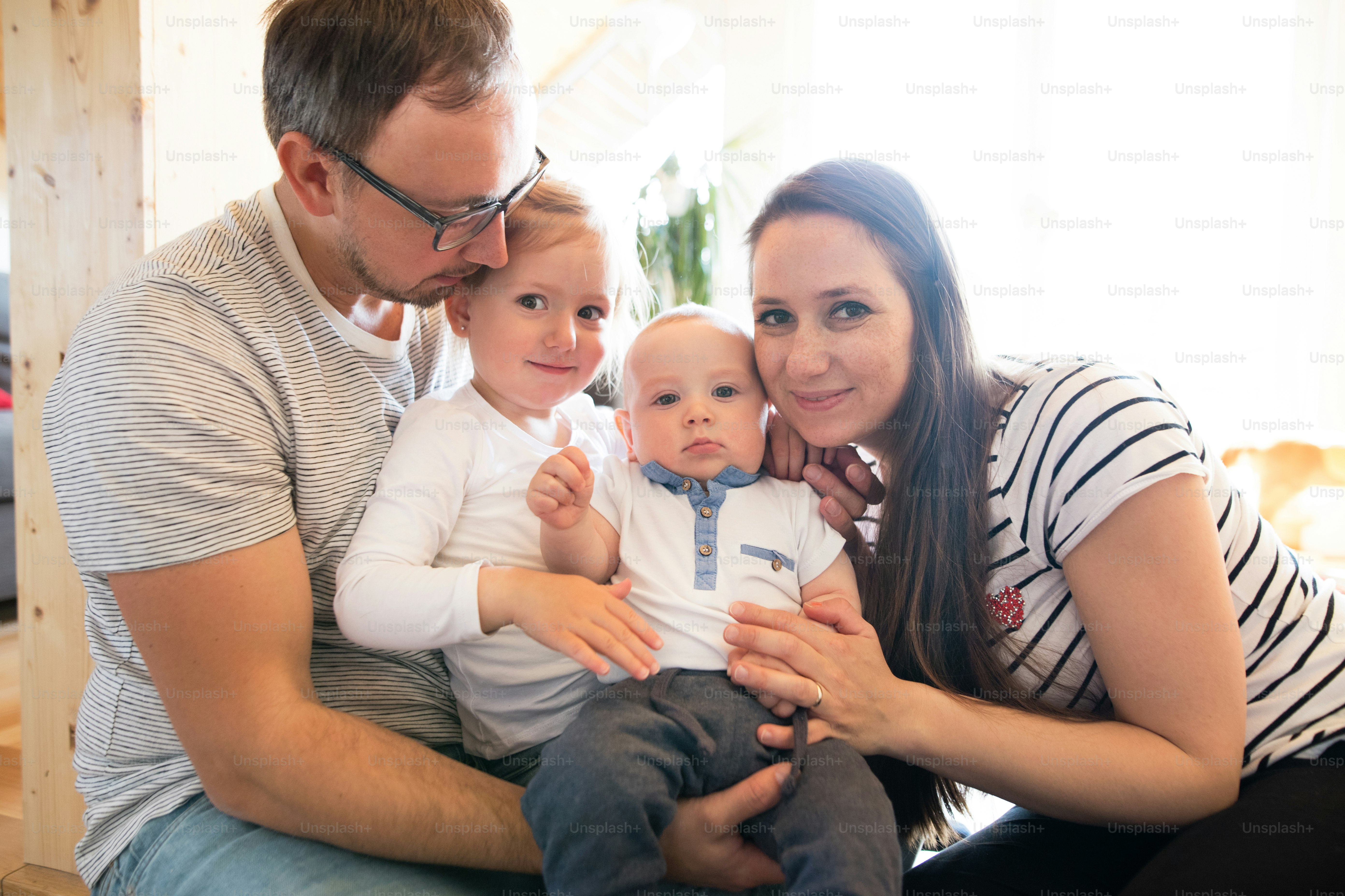 Beautiful young parents at home holding their cute son and daughter in the arms.