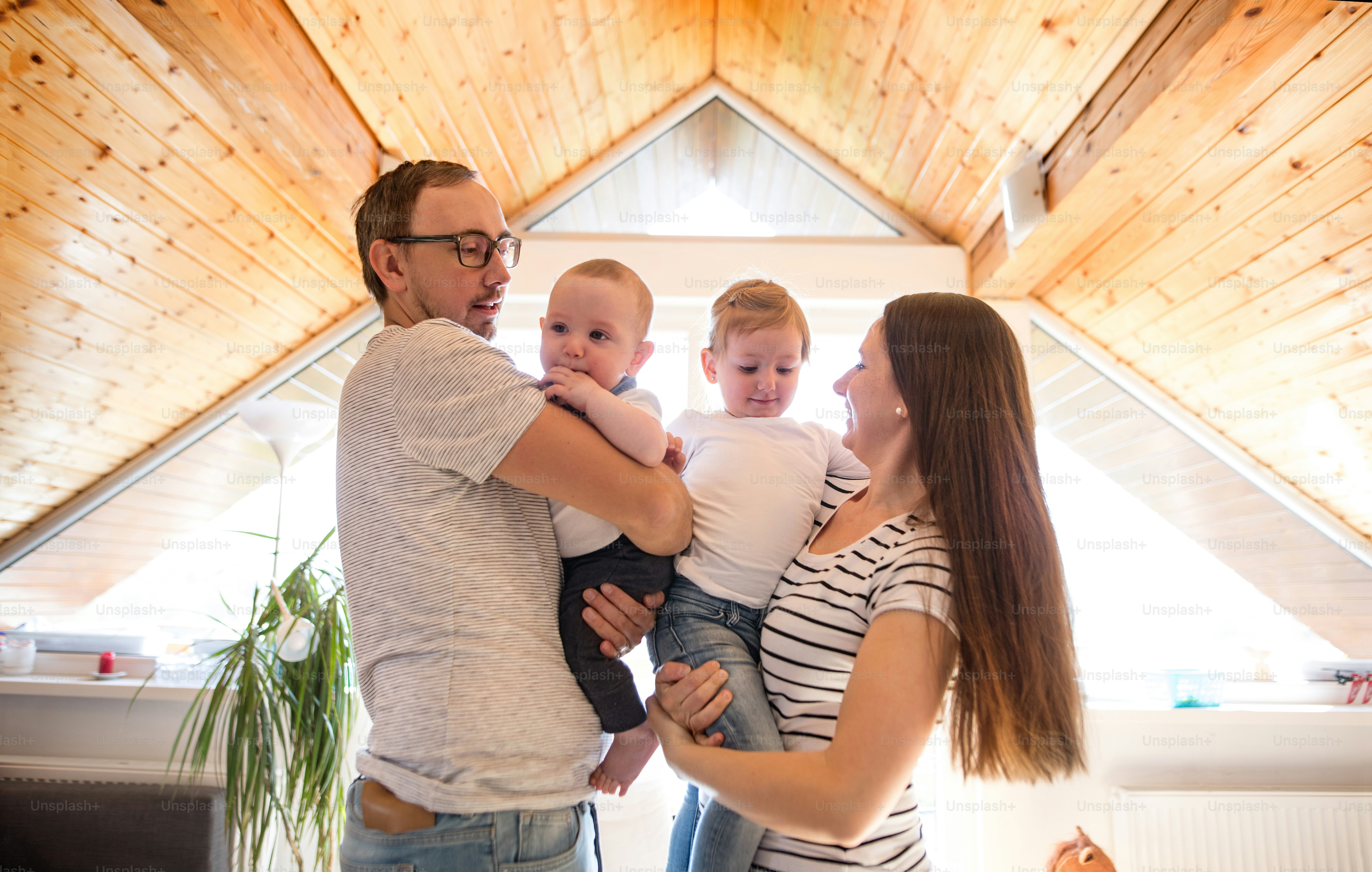Beautiful young parents at home holding their cute son and daughter in the arms.